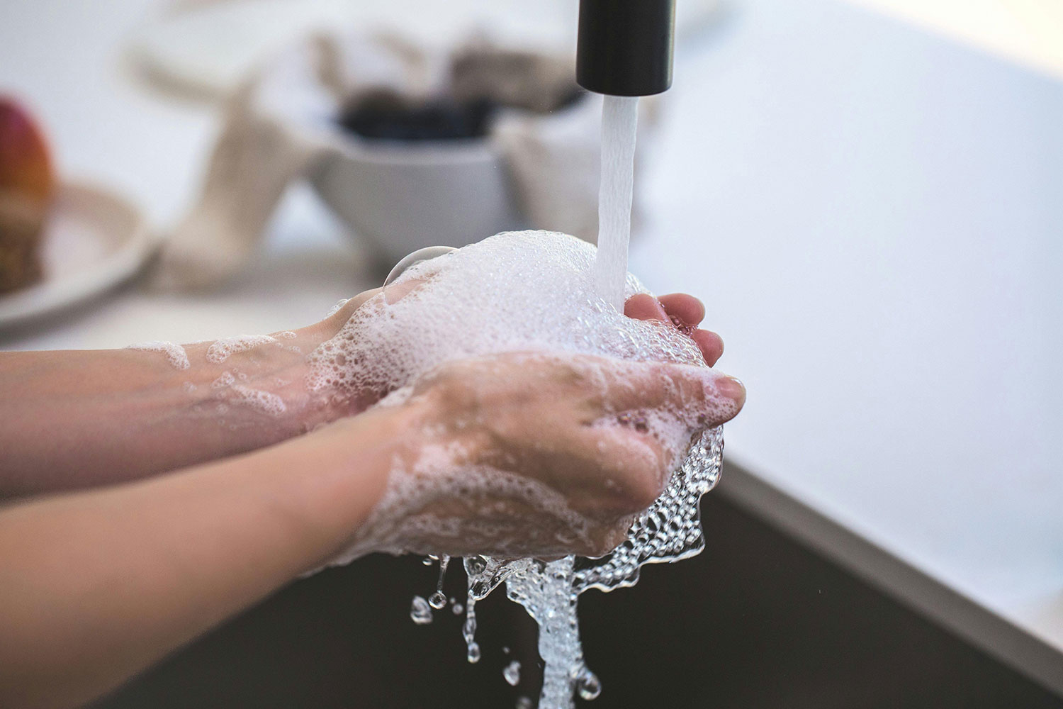 Mãos lavadas com sabão, com bactérias sendo eliminadas. Prevenção contra infecções.